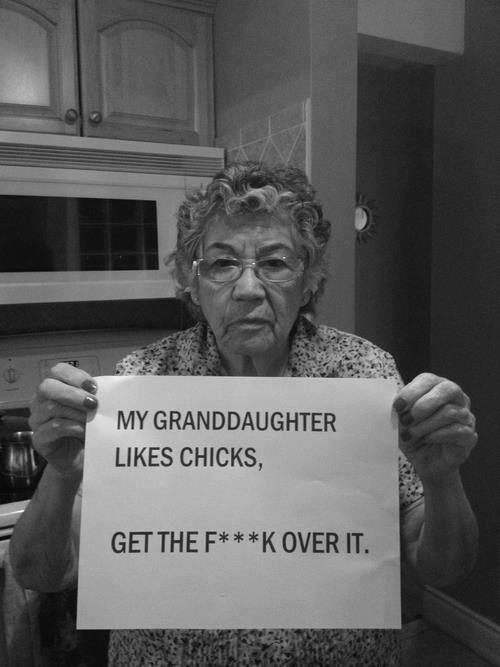 Man sieht eine ältere Frau, sie hält ein Papier, darauf steht "My Grandmother likes Chicks, Get the F**k over it"