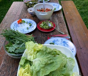 Man sieht einen Holztisch mit Tellern und Schüsseln mit Salat und Gemüse darin, auch essbaren Blüten.